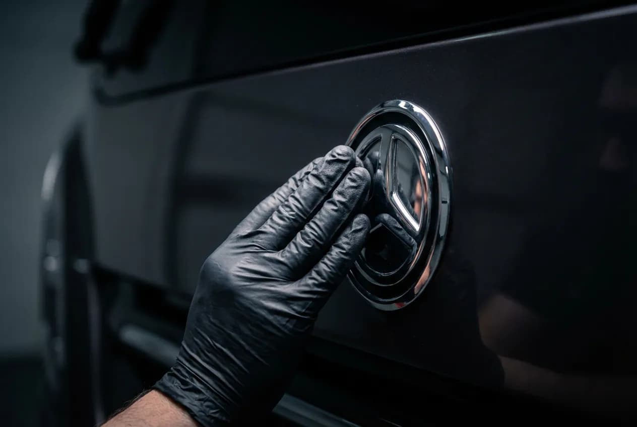 Gros plan d'une main gantée qui lustre un détail chromé sur la carrosserie d'un camping-car, créant un reflet parfait.