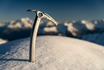 Piolet de randonnée planté dans la neige immaculée au sommet du Dôme de la Lauze, symbolisant l'ascension réussie.