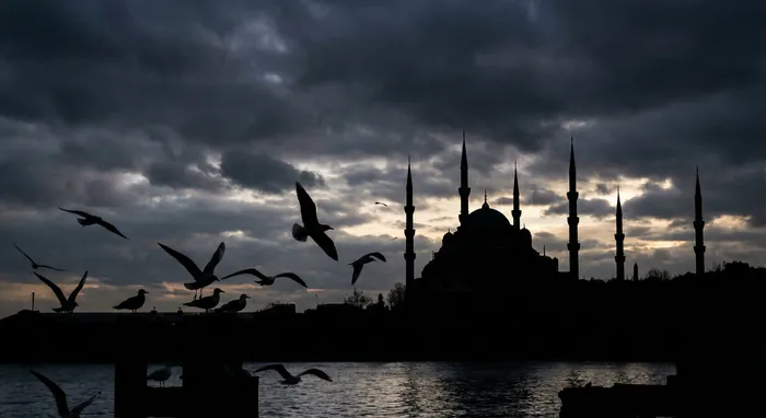 Silhouette de la Mosquée Bleue et envol de mouettes sous un ciel dramatique à Istanbul.