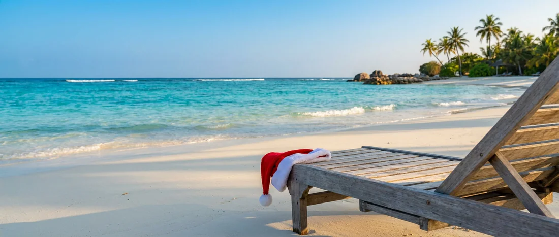 Plage paradisiaque de sable blanc avec eau turquoise et un bonnet de Père Noël sur un transat.